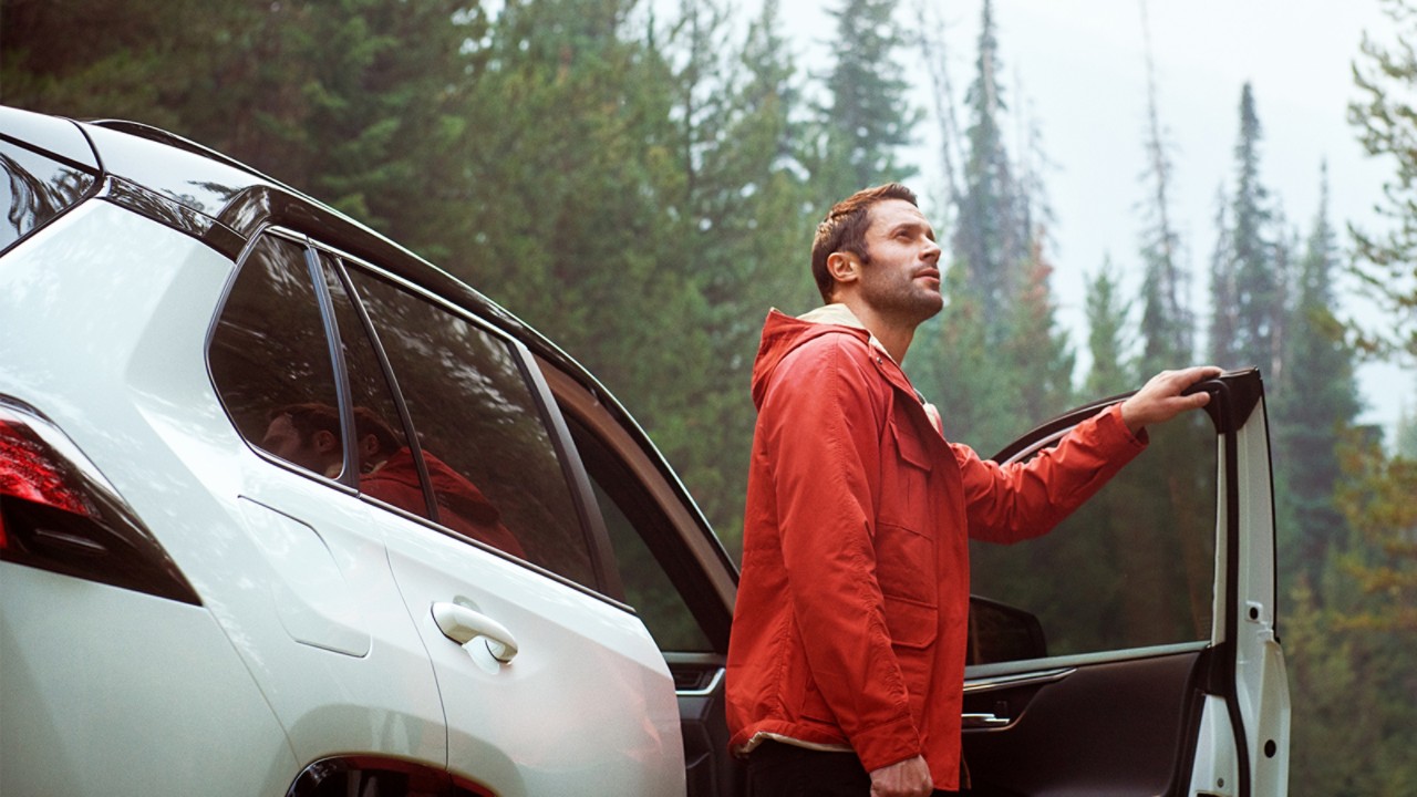Young man in red jacket stepping out of PHEV contemplating nature