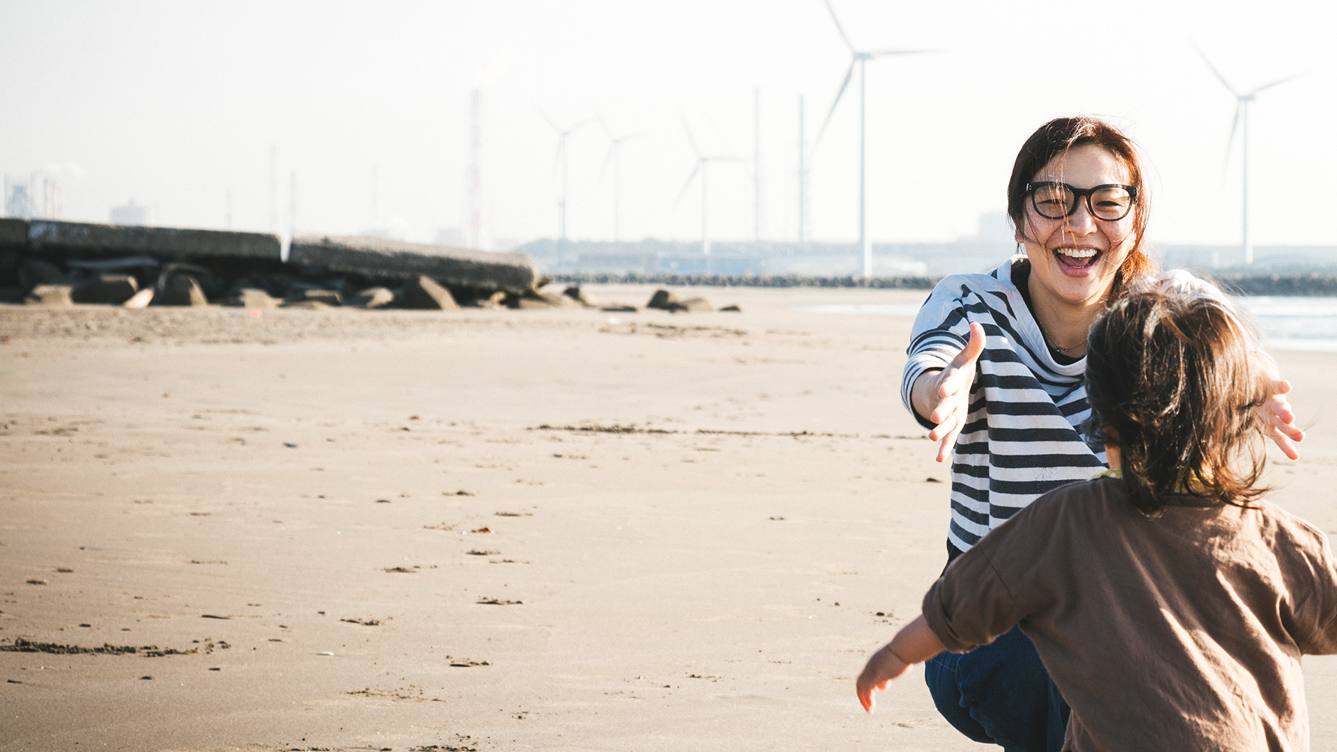 Kid running to mother on a beach with windmills